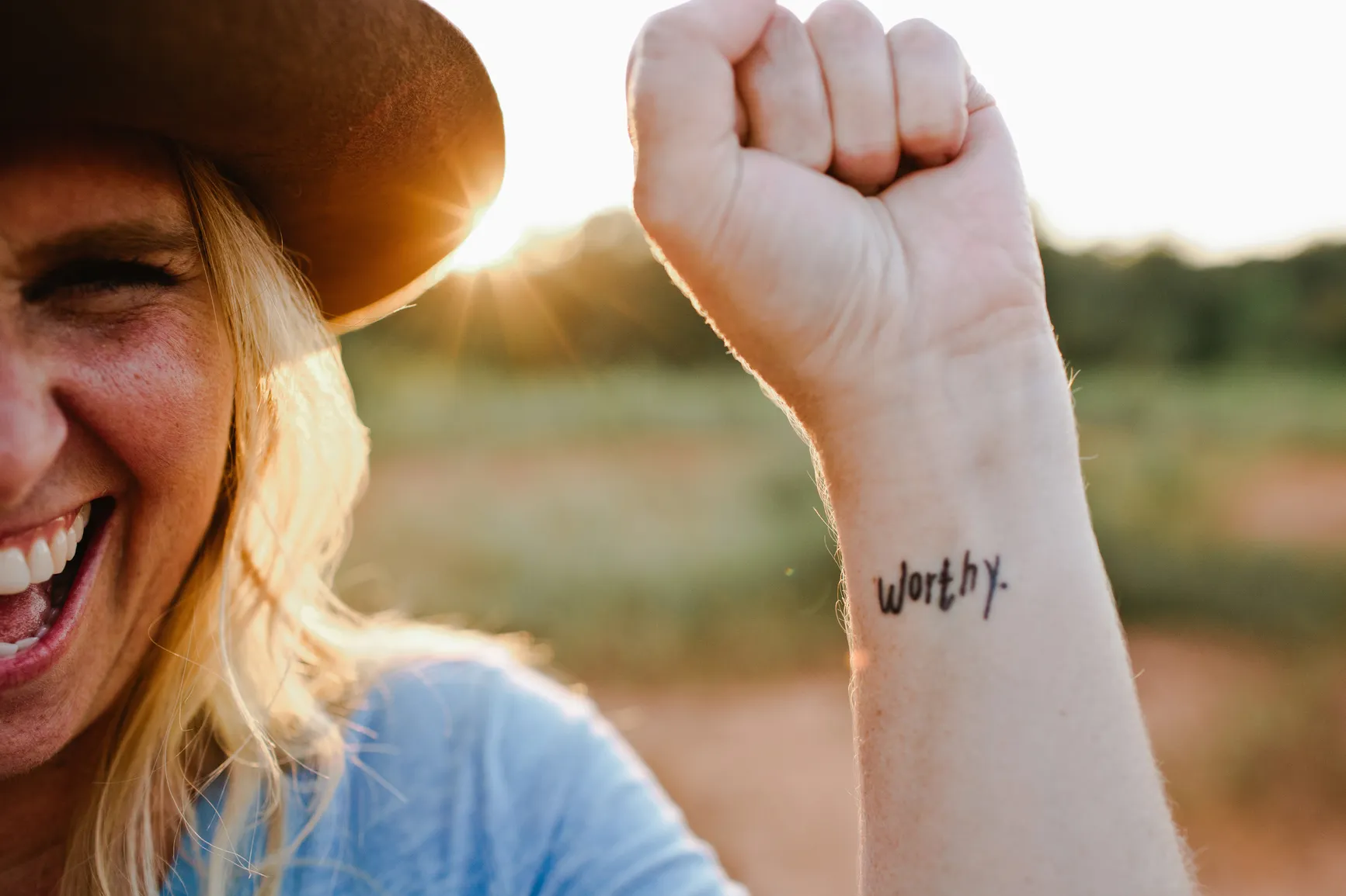 This is an image of a woman holding her arm up with the word ‘Worthy’ tattooed on it