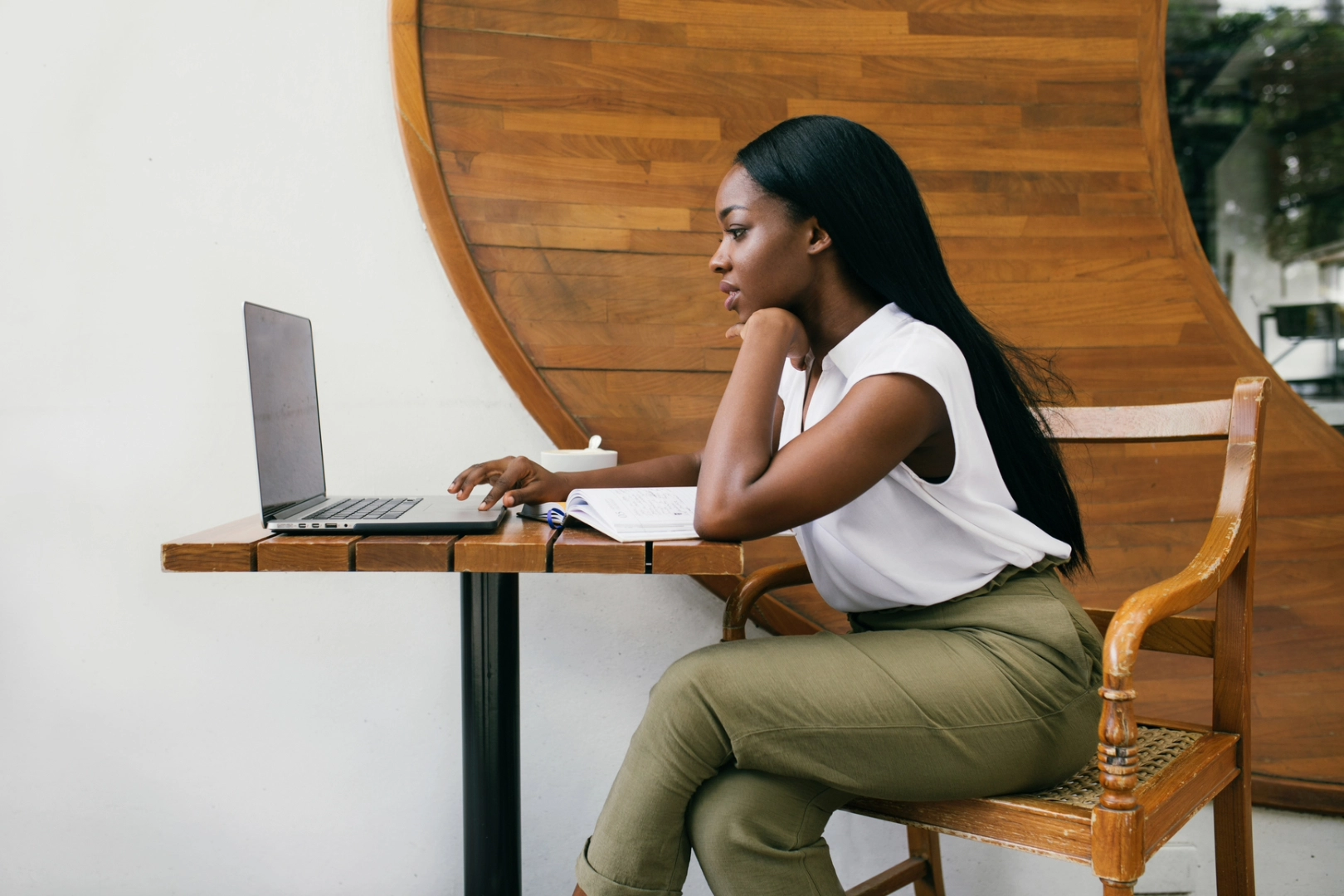 A woman sits at her a wooden table, typing on her computer, considering the angel numbers for her career.