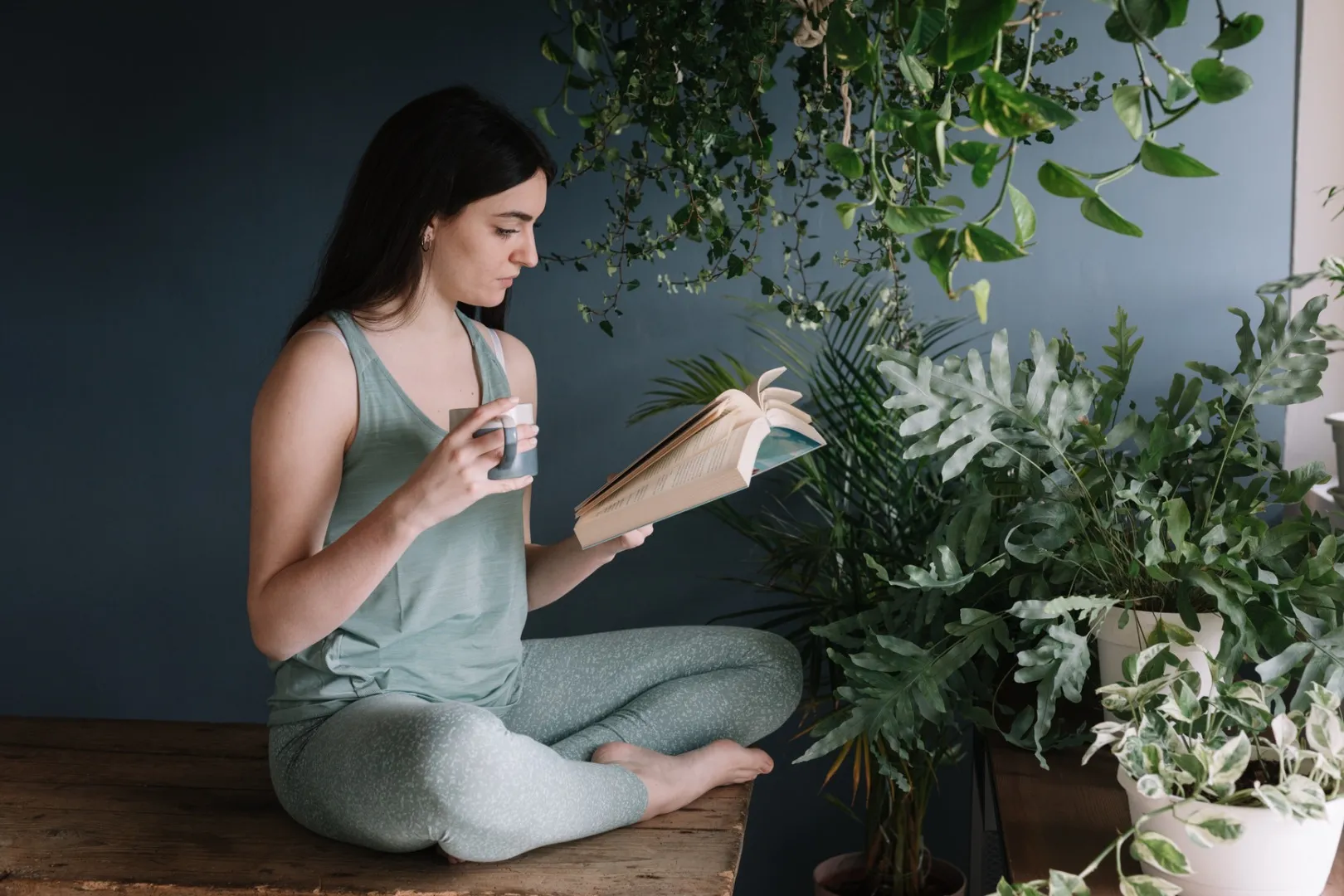 A young woman sits and reads a book while drinking a prepared herbal tea for her dominant dosha type.