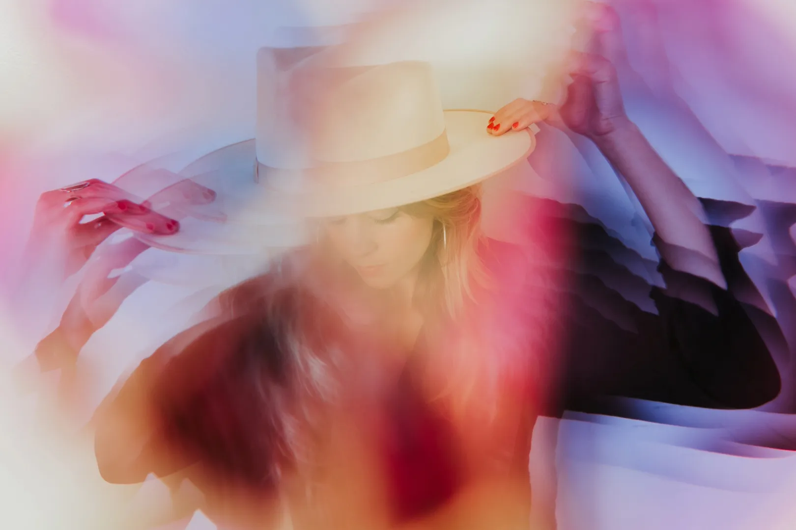 Woman in a black shirt holds a white hat on her head, photographed with her aura colors surrounding her.