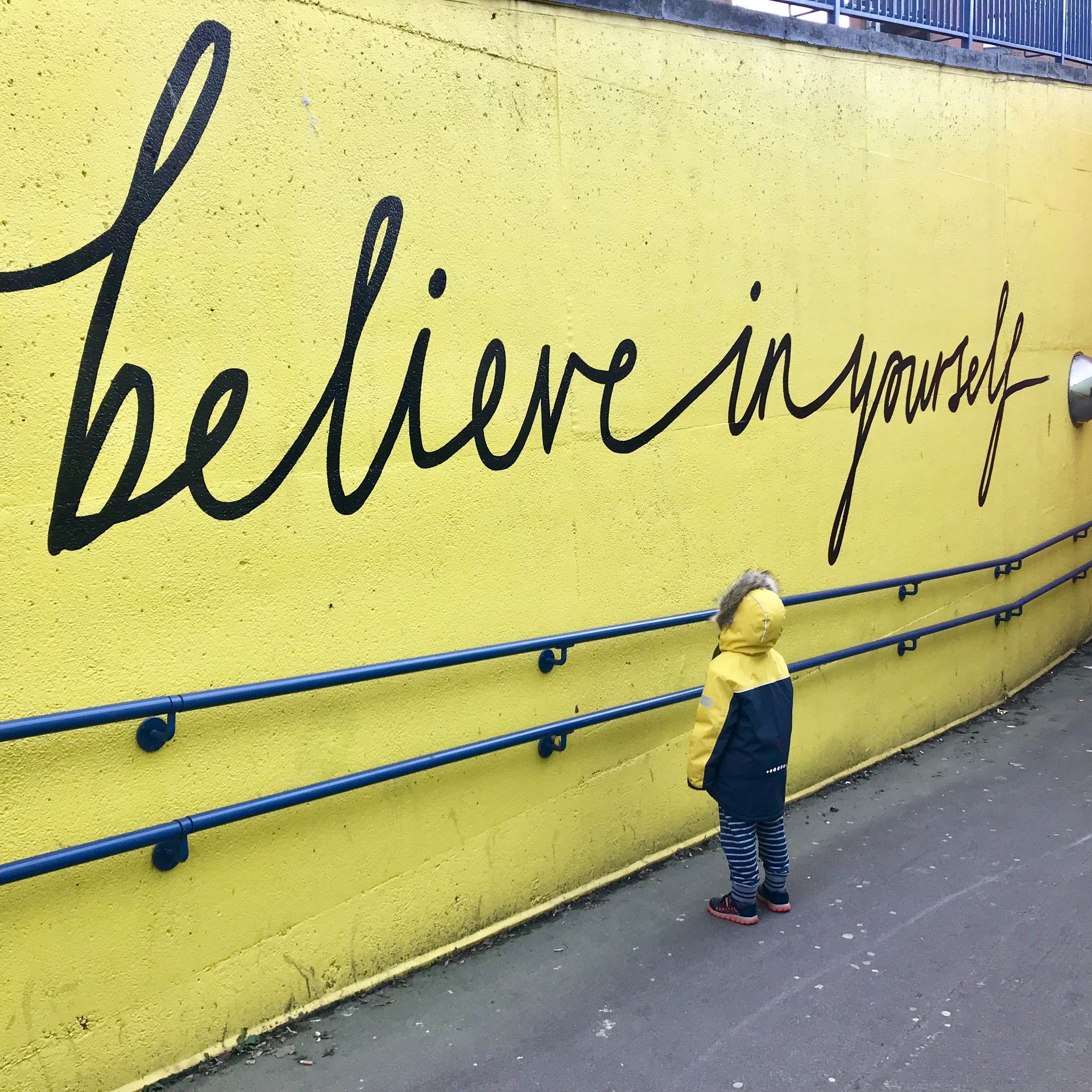 Child looking at a bright yellow mural that reads Believe in Yourself