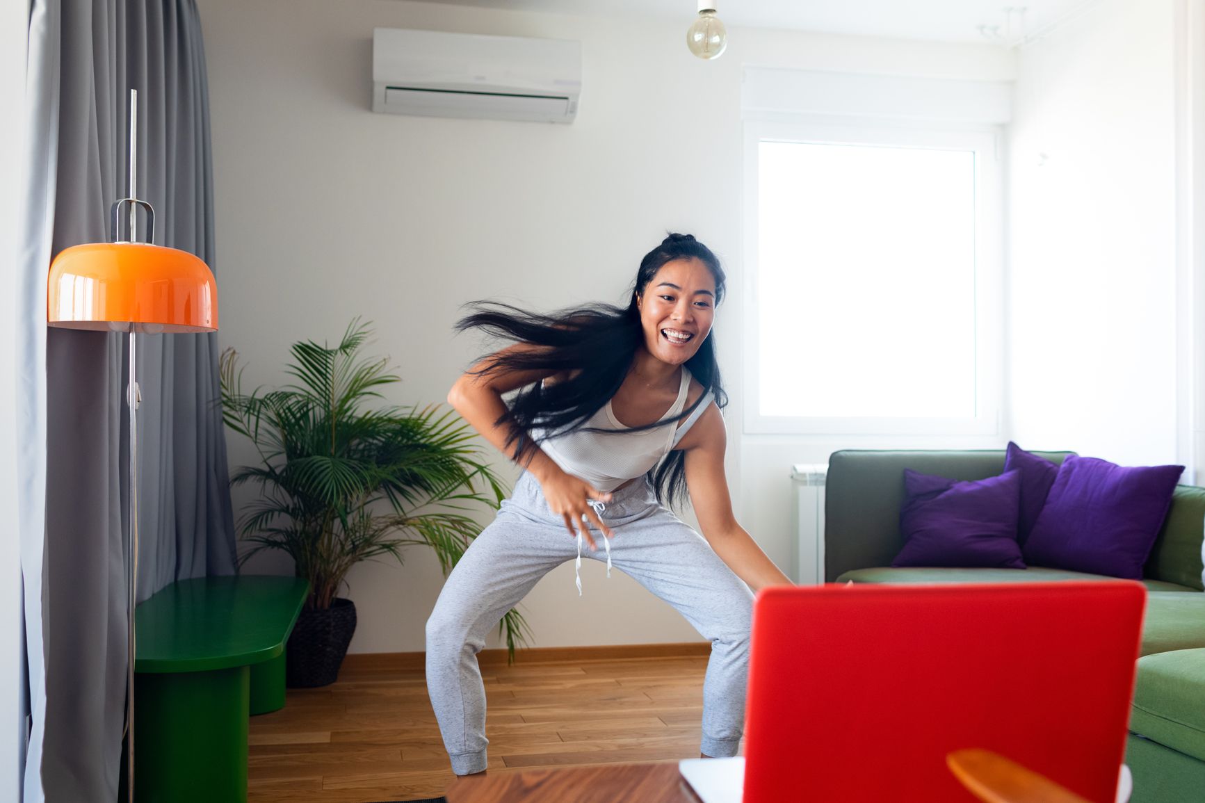 Happy woman dances alone in her living room while standing in front of her computer