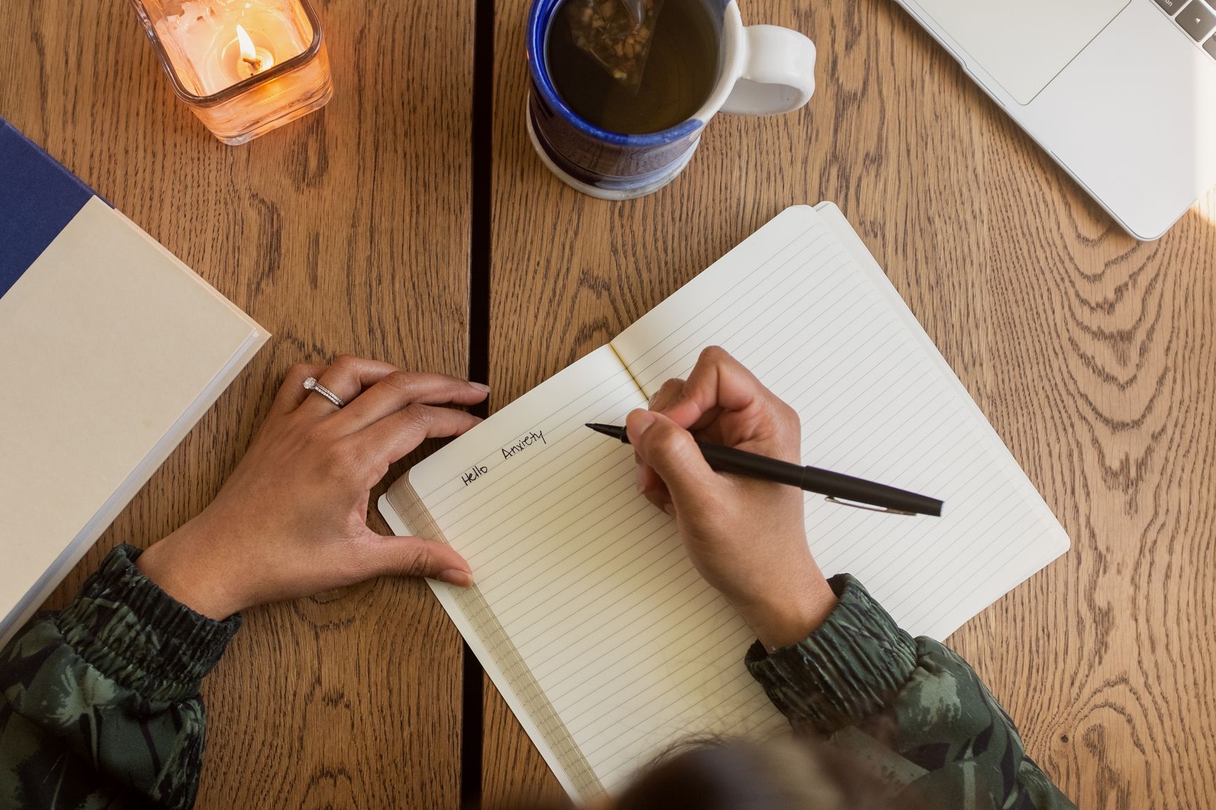 Photo of hands holding a pen and a lined paper journal with the words 'Hello Anxiety' written on the page