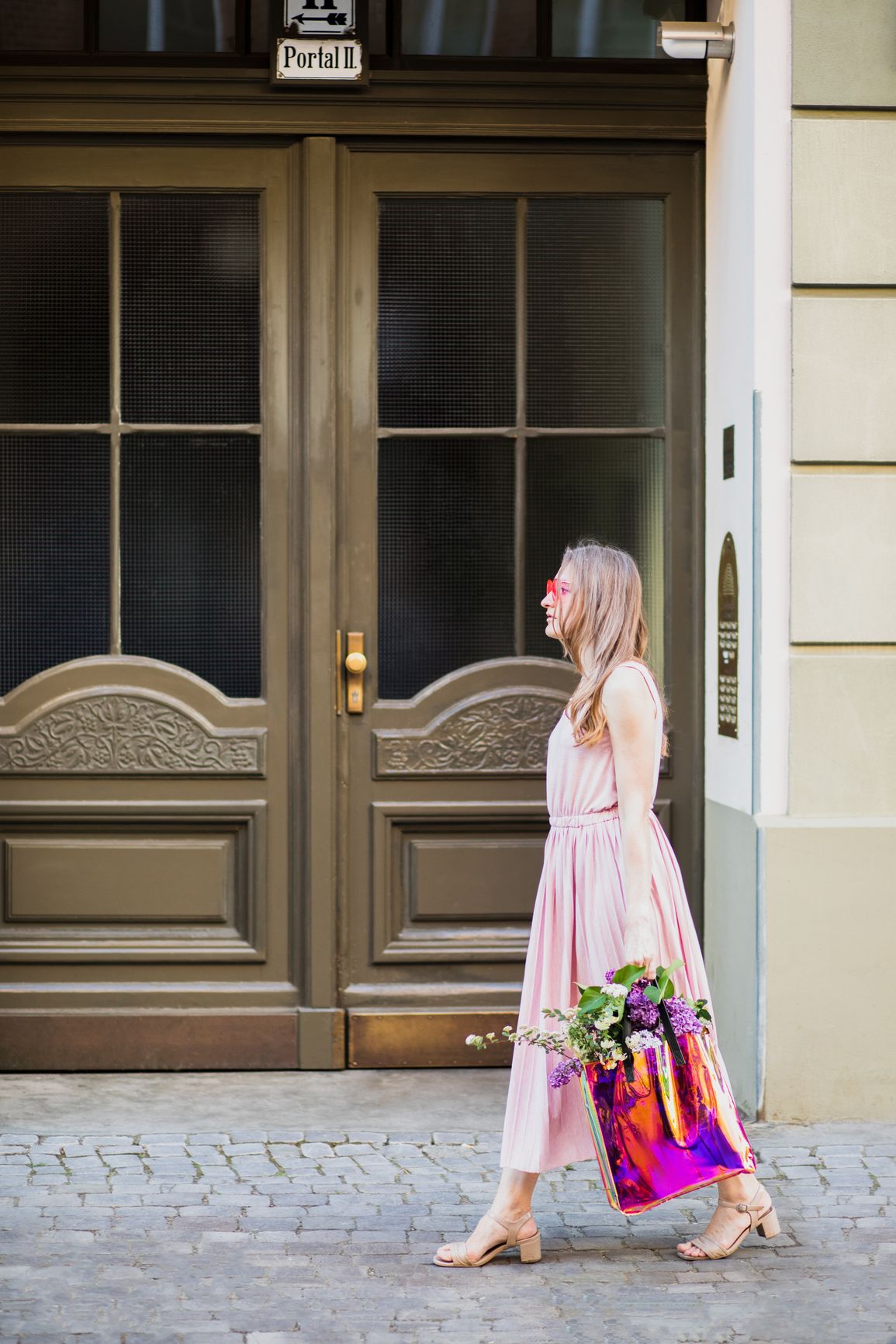 Woman wearing a pink dress walks down a city street carrying a tote bag full of colorful flowers 