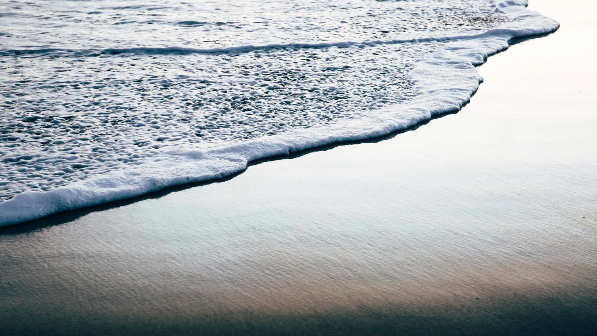 Crashing of waves rolling over the sand on a beach at sunset