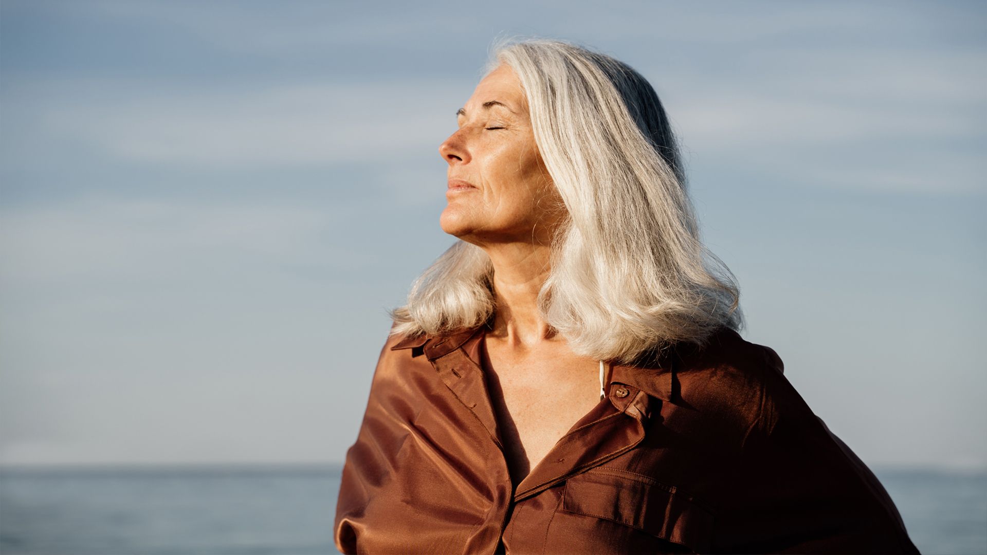 Mature Woman outdoors enjoying the beach. Her eyes are closed, and her head is turned sideways.