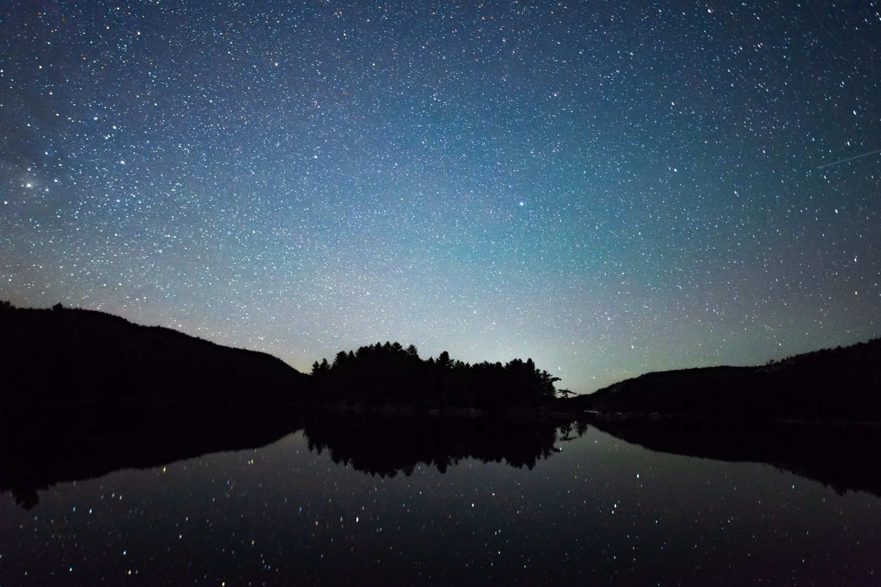 Relaxing photograph of a lake at night with the stars brightly lit above 