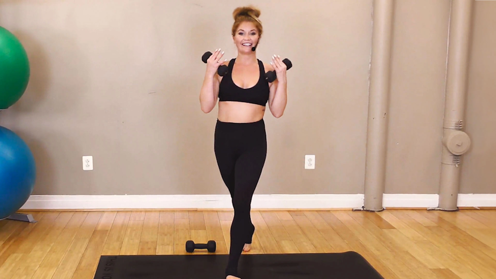 Yoga instructor Bridgette Hall holding a pair of light dumbbells while demonstrating a power yoga workout.