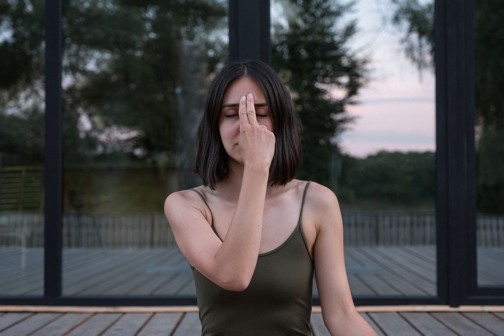 Woman in activewear with dark hair touching Third Eye Chakra and meditating with closed eyes during yoga session outdoors 