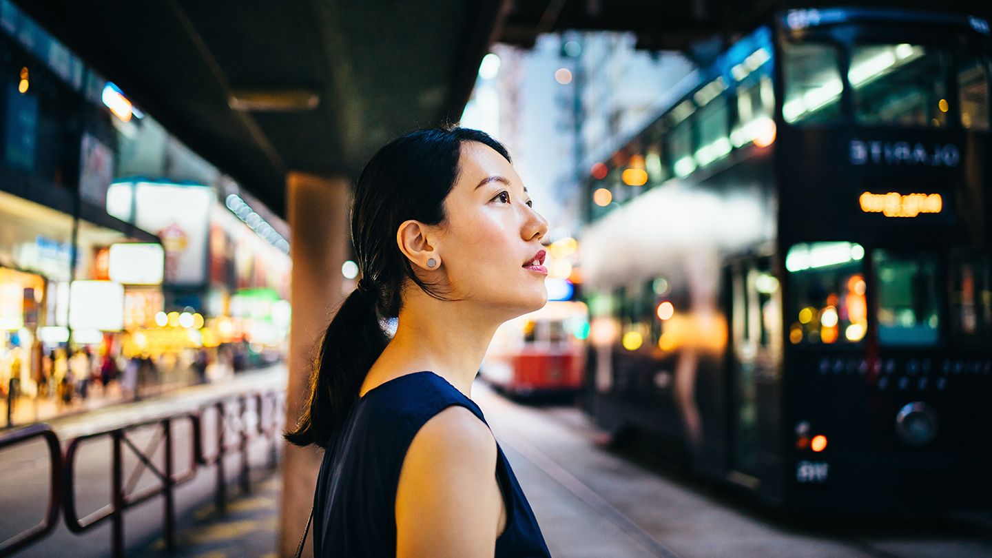 Young Asian woman traveller visiting and exploring busy city street looking up with curiosity