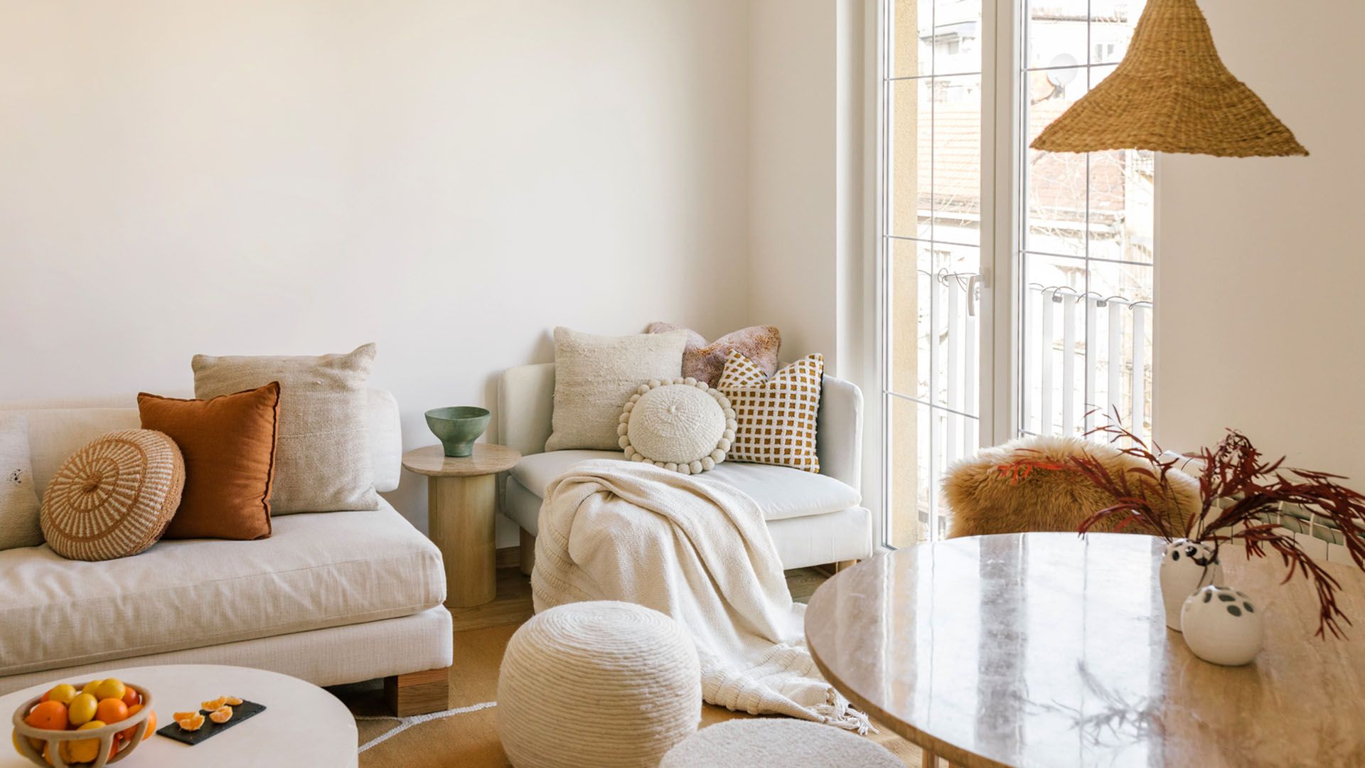 Bright, sunny interior room of an apartment decorated with creams, whites, browns, and warm accent pieces.