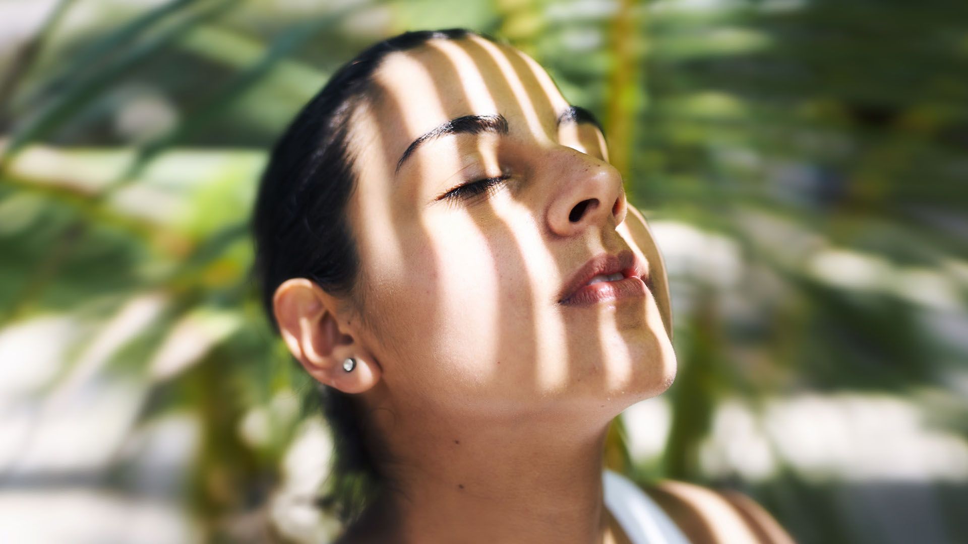 Woman outdoors, eyes closed and the sun on her face, practices mindfulness and breathing exercises.