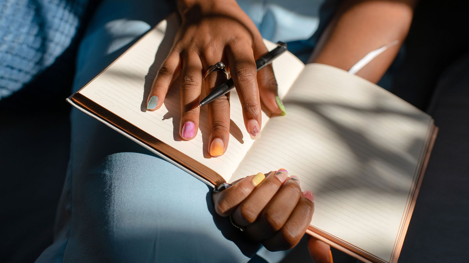 Woman's hands with nails painted in colorful shades, holds a pan and an open blank journal on her lap