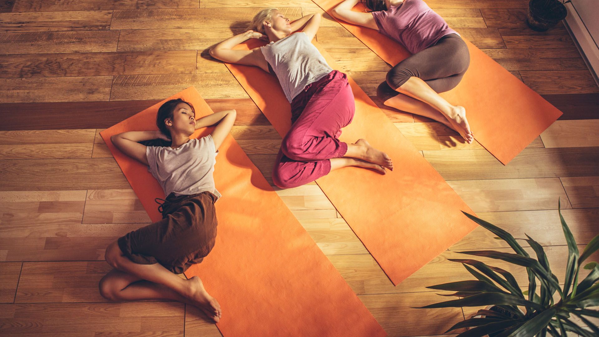 Three women doing yoga spinal twists while laying down on orange mats