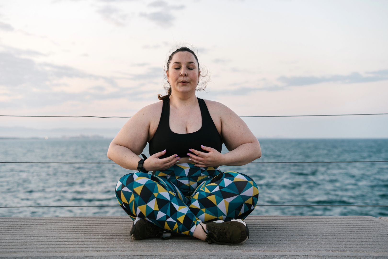 A woman sits outside, eyes closed and doing deep breathing in order to help reset her nervous system to de-stress.