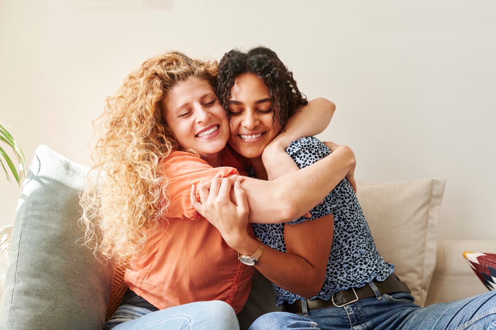 Two empath friends hug warmly as they sit together on the couch.