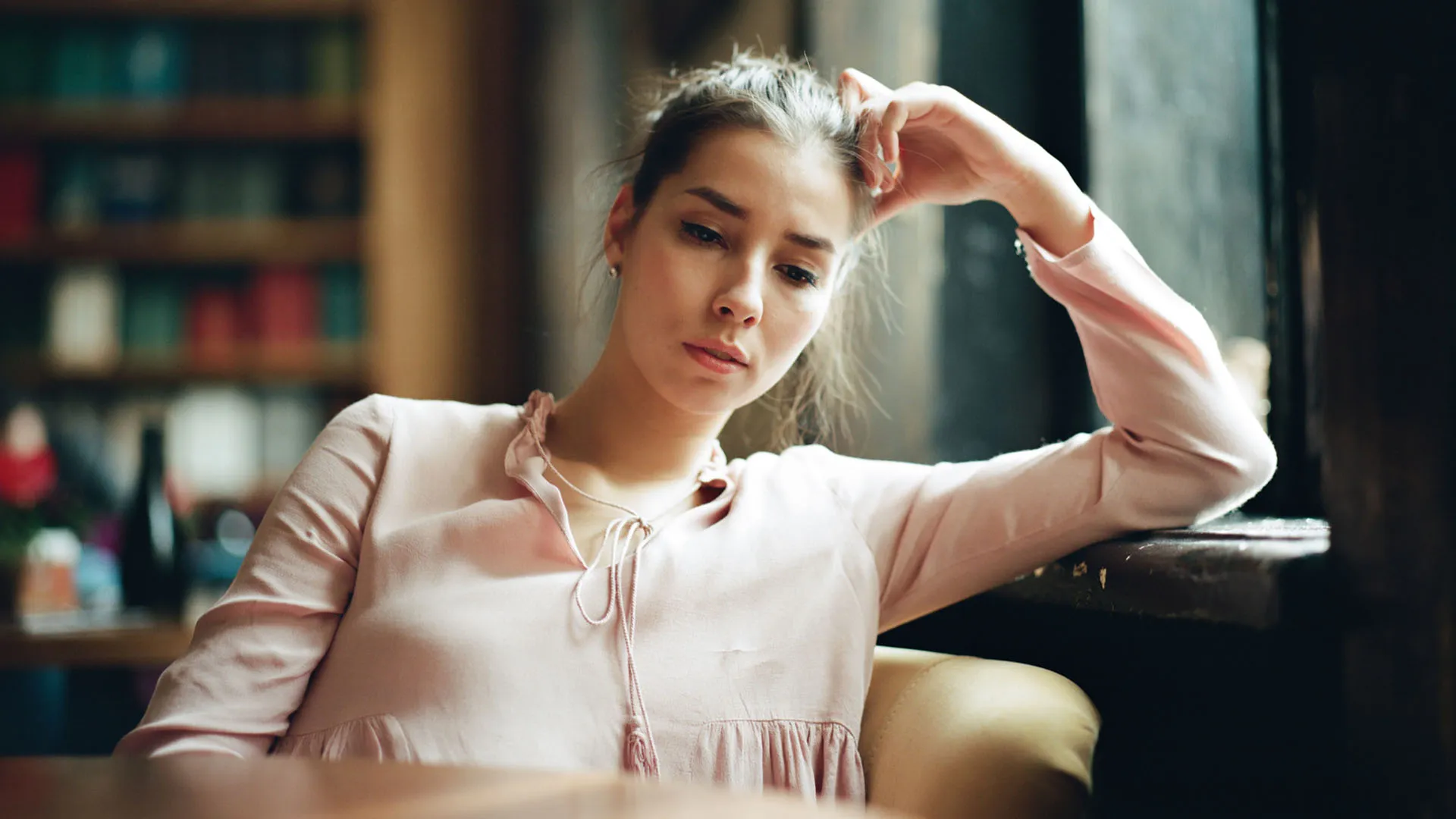 Woman with melancholy expression on her face sits alone in a cafe, staring down at the empty table in front of her.