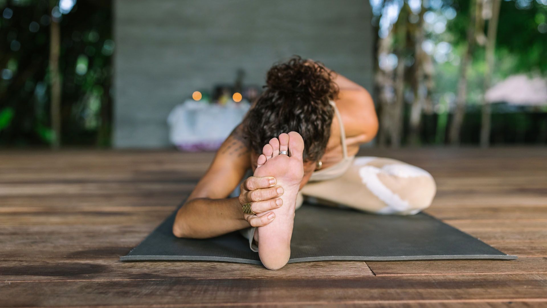 A woman leans forward and does a yoga stretch on a black mat.