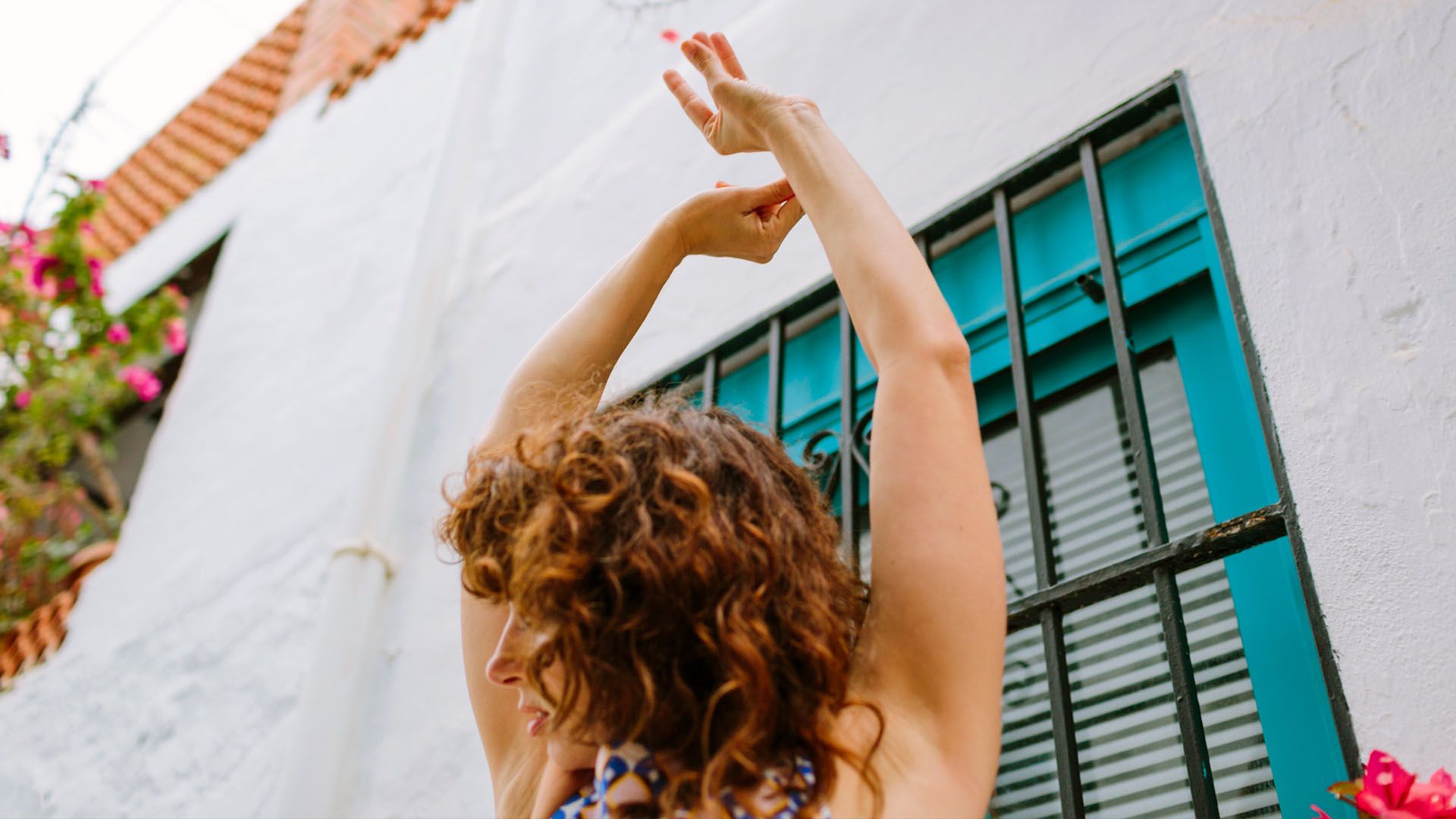 Curly haired woman shown from the back holds her with arms up as she dances in the street