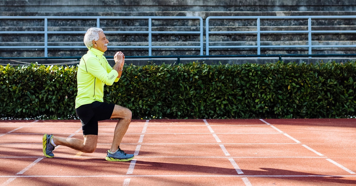 Older man doing primal movement lunges outdoors on a track to relieve minor aches and pain and build muscle strength.