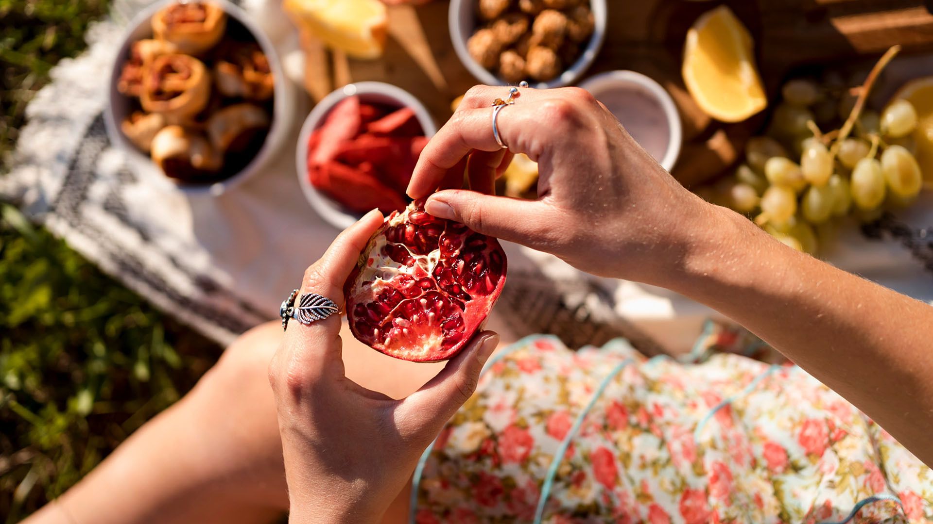 Top view of a picnic blanket and a close-up view of a woman's hands holding a sliced pomegranate.