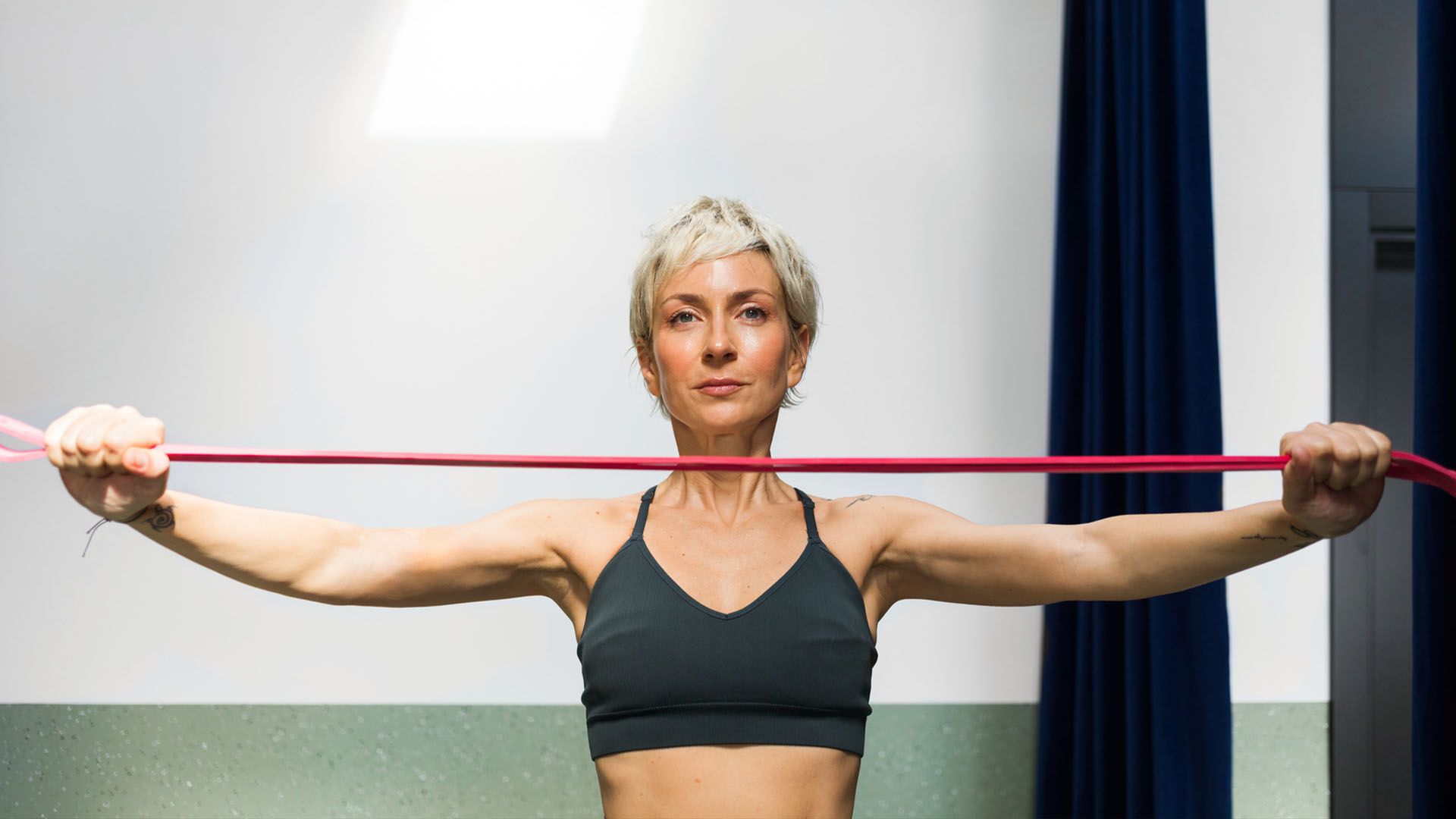 Woman with white hair and a short pixie cut hairstyle uses a stretching resistance band to exercise.