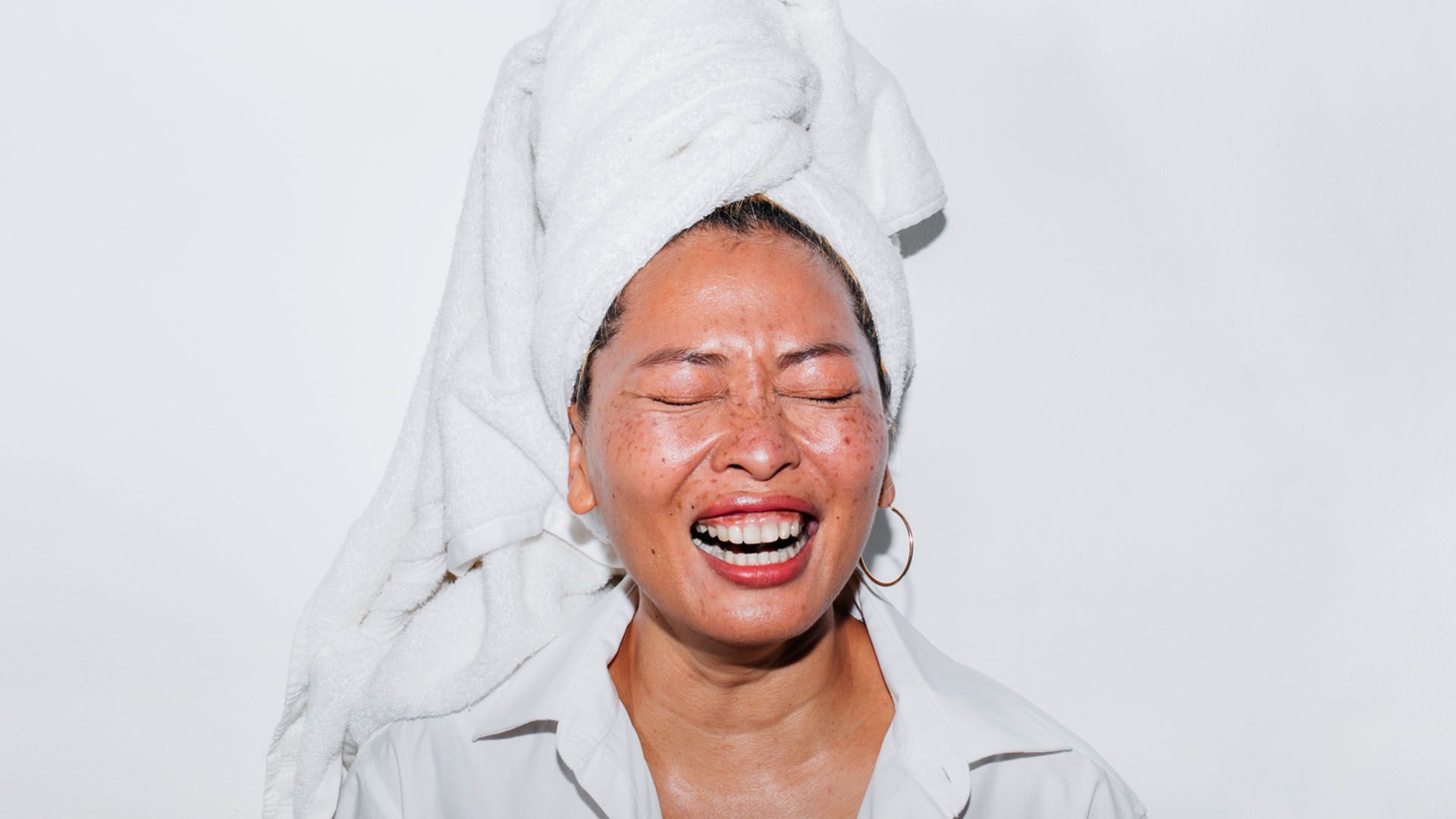 Asian woman laughing during skincare routine with towel on head