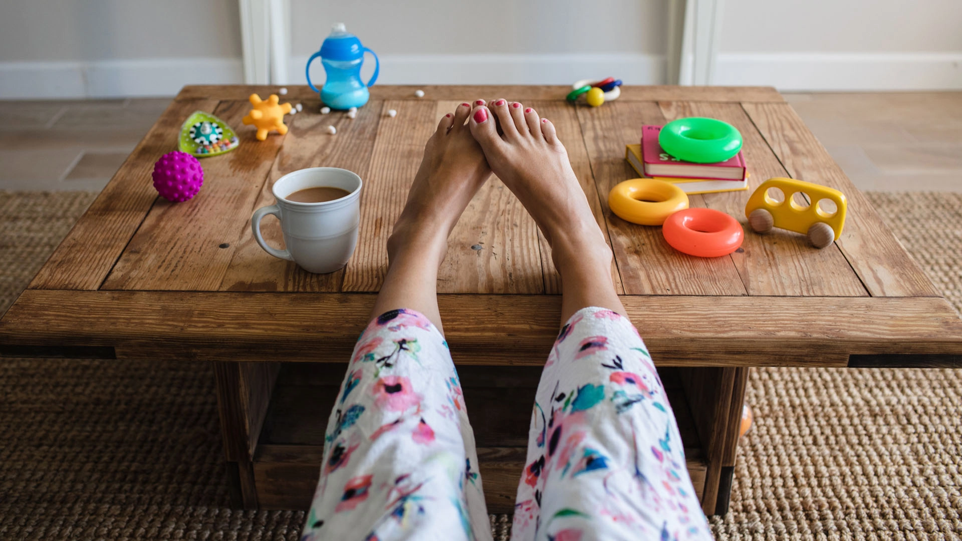 Shot of a woman’s legs up on a coffee table that holds a cup of coffee and baby toys, savoring being alone during her baby's nap.