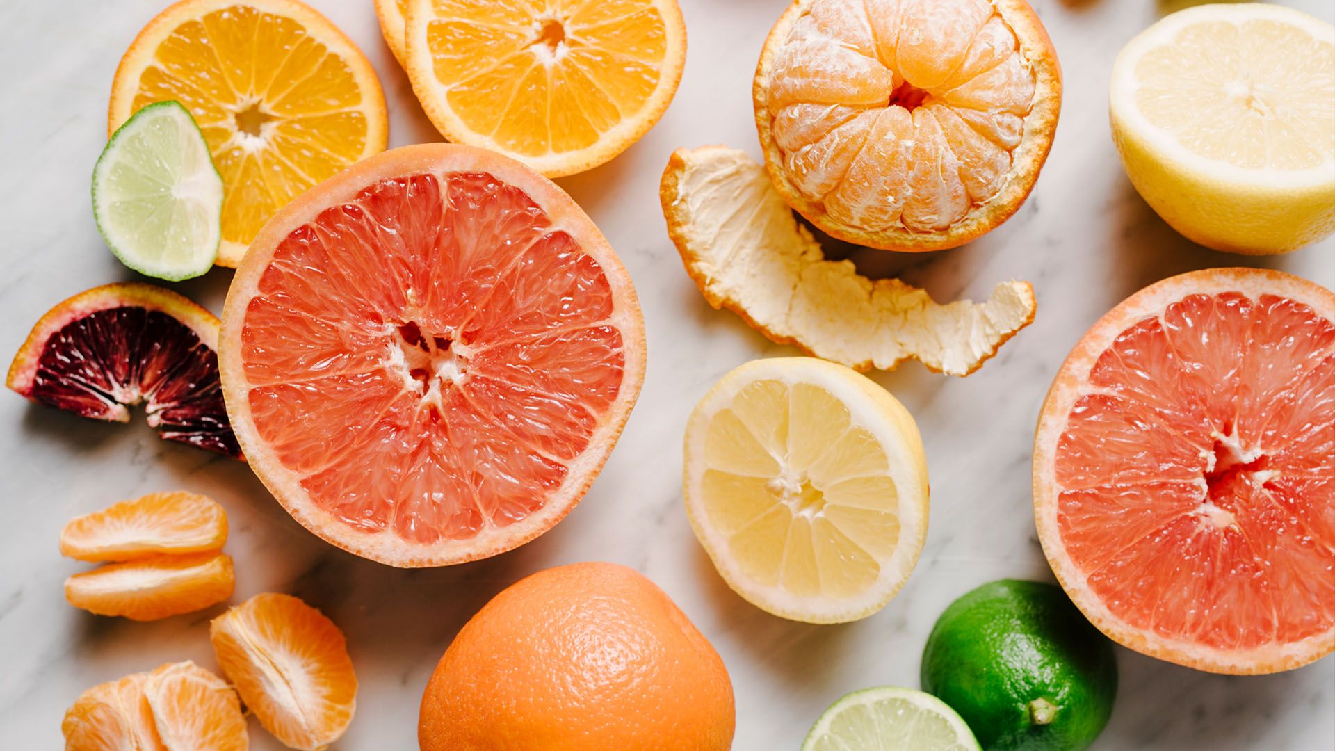 Colorful array of sliced citrus flatlay; ruby grapefruits, oranges, limes, and a blood orange slice