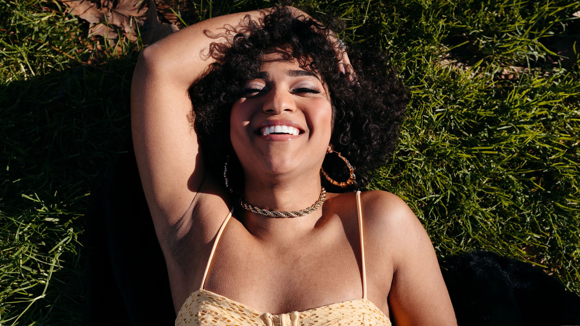 Woman lays in a field, smiling and looking happy as she recites a body-positive affirmation.