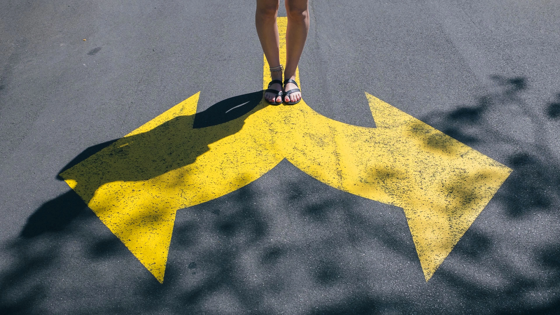 Legs of a woman standing in the middle of the street on a yellow road sign of two arrows, making a choice which direction to turn