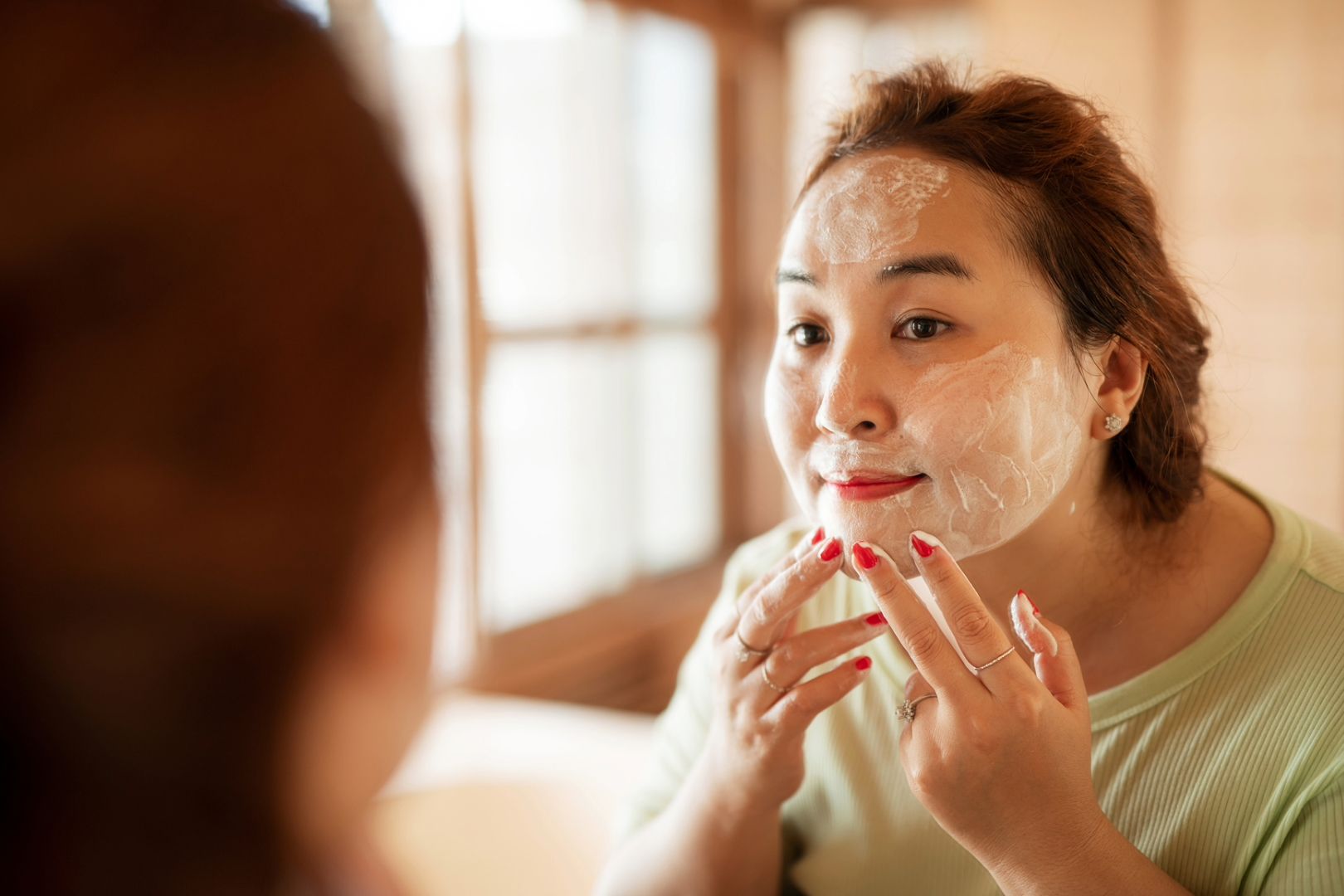 Woman taking a break from her skincare routine by practicing a skin reset looks in the mirror while washing her face.