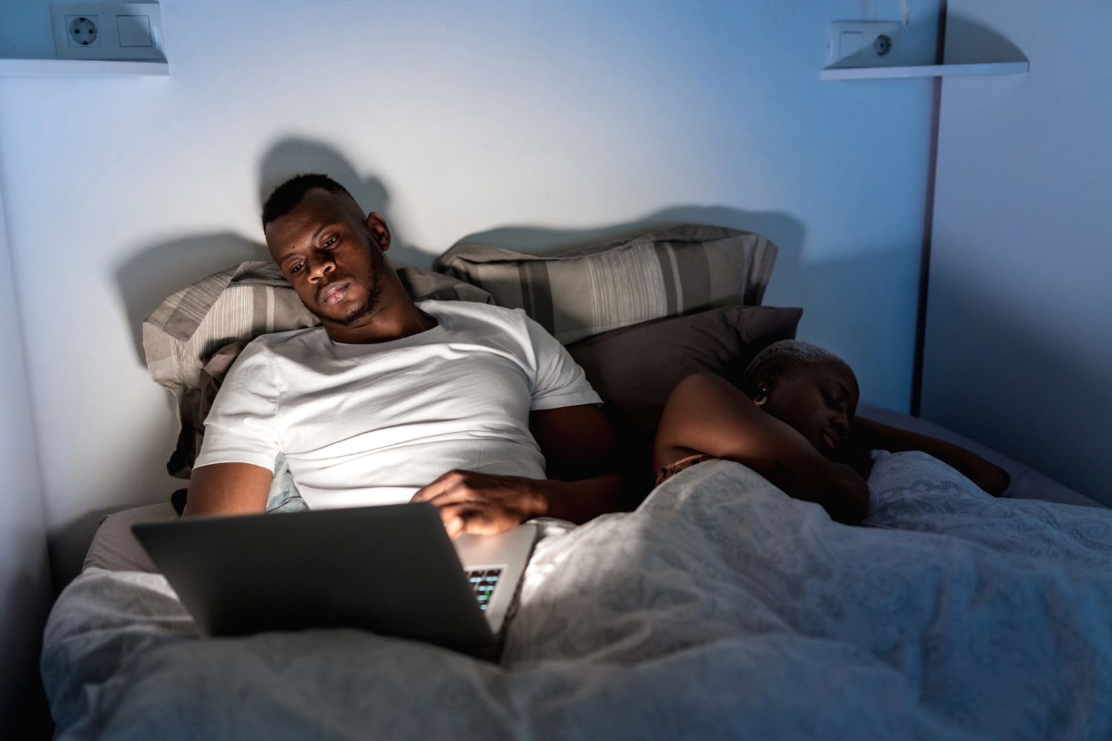 While his partner sleeps, a man watches TV on his laptop computer. Do their different sleep schedules require a sleep divorce?