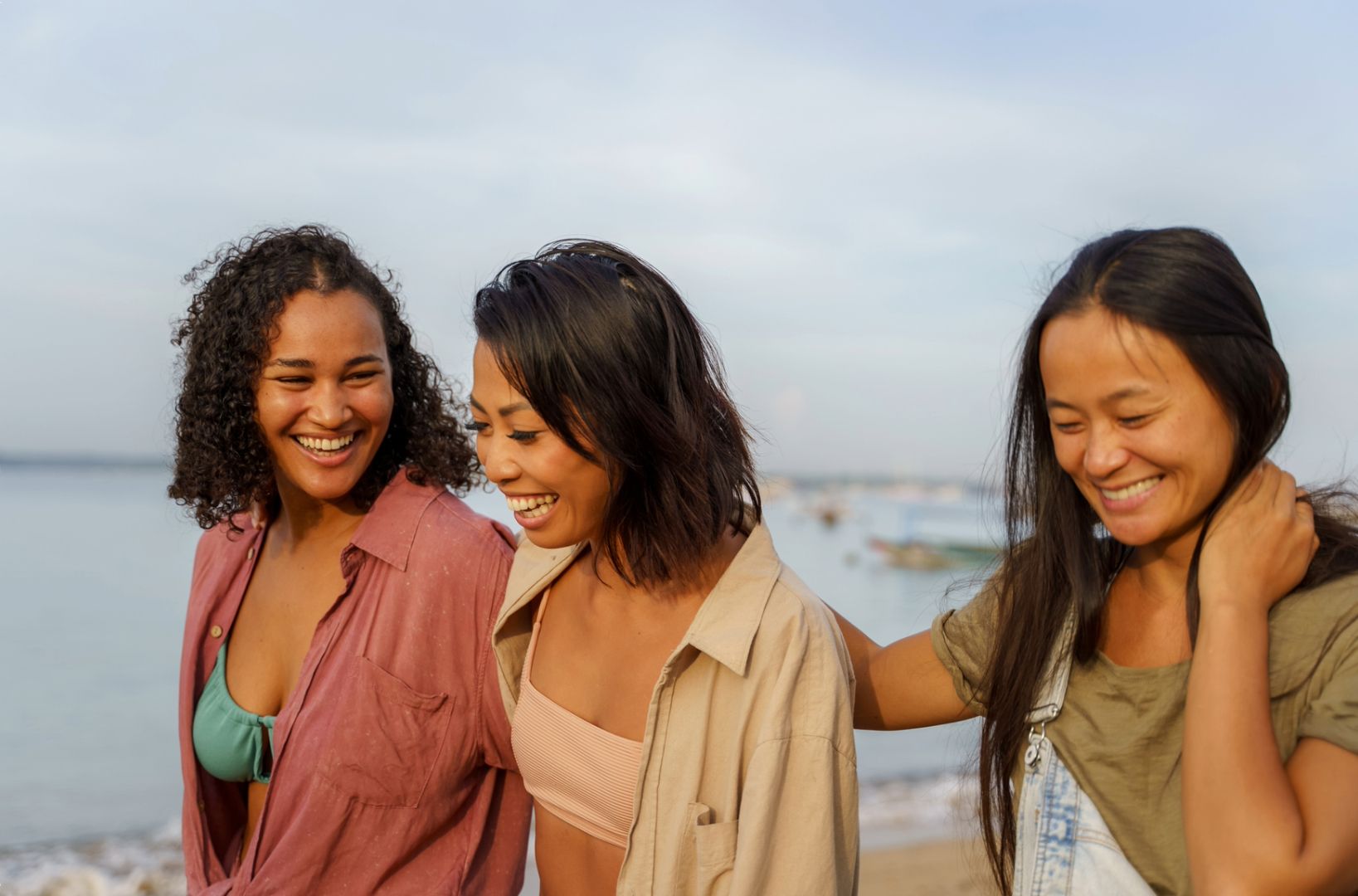 Three smiling women walk along the beach offering each other genuine optimism and support.