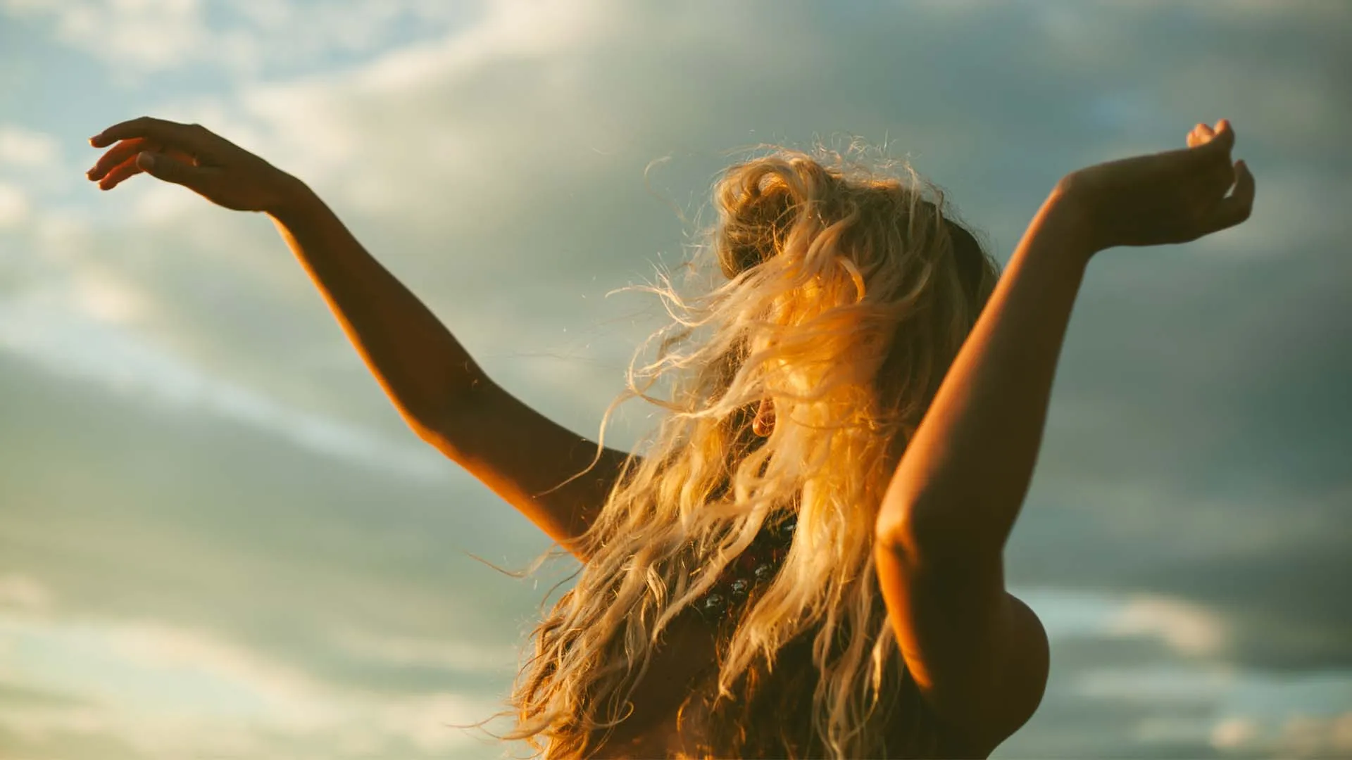 A white woman dances joyfully at sunset.