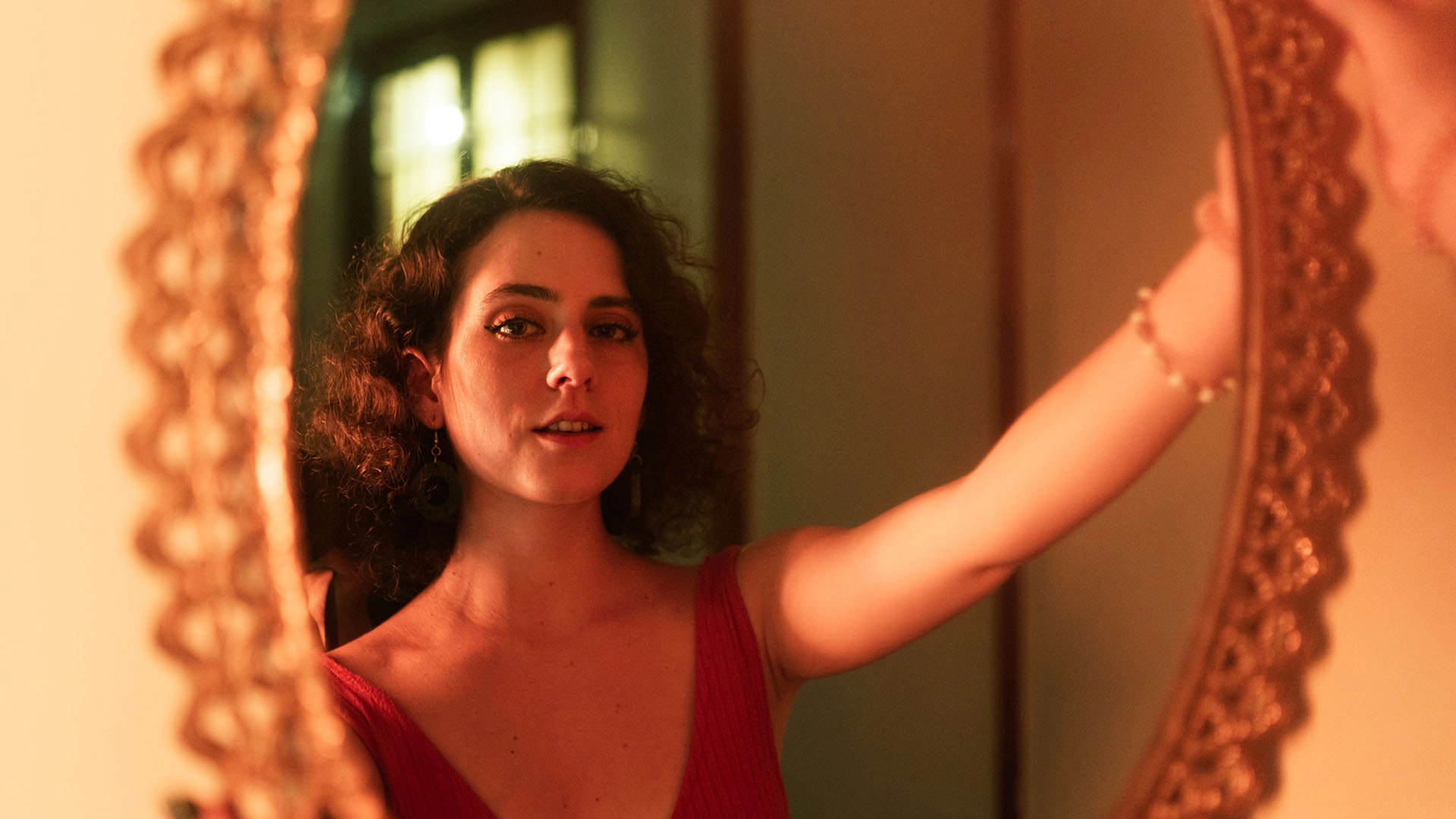 Woman wearing a red dress admires herself in a mirror.