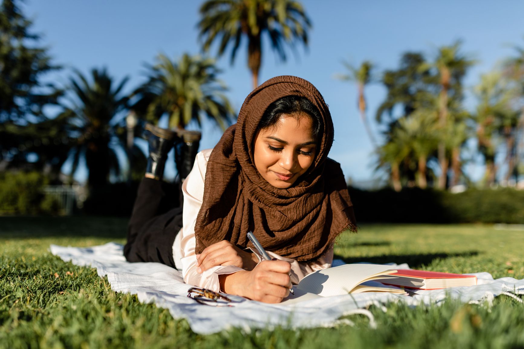 Smiling woman on blanket in a park writes in a journal 