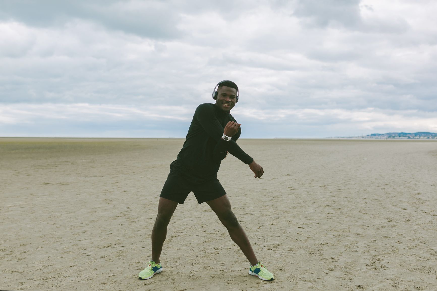 Man wearing workout clothing stretches on the beach while listening to headphones 