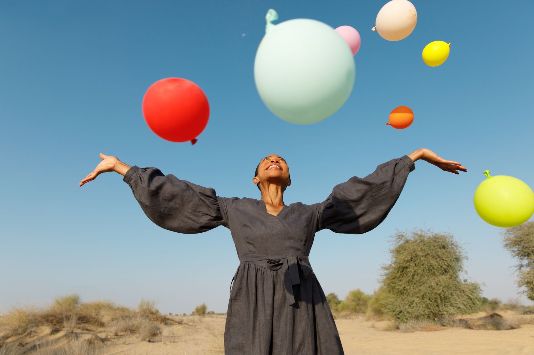 A woman stands outside looking happy surrounded by colorful balloons above her 