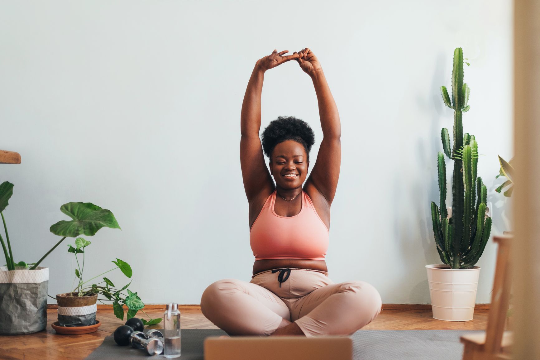 Woman sits on a yoga mat on the floor and stretches arms overhead 