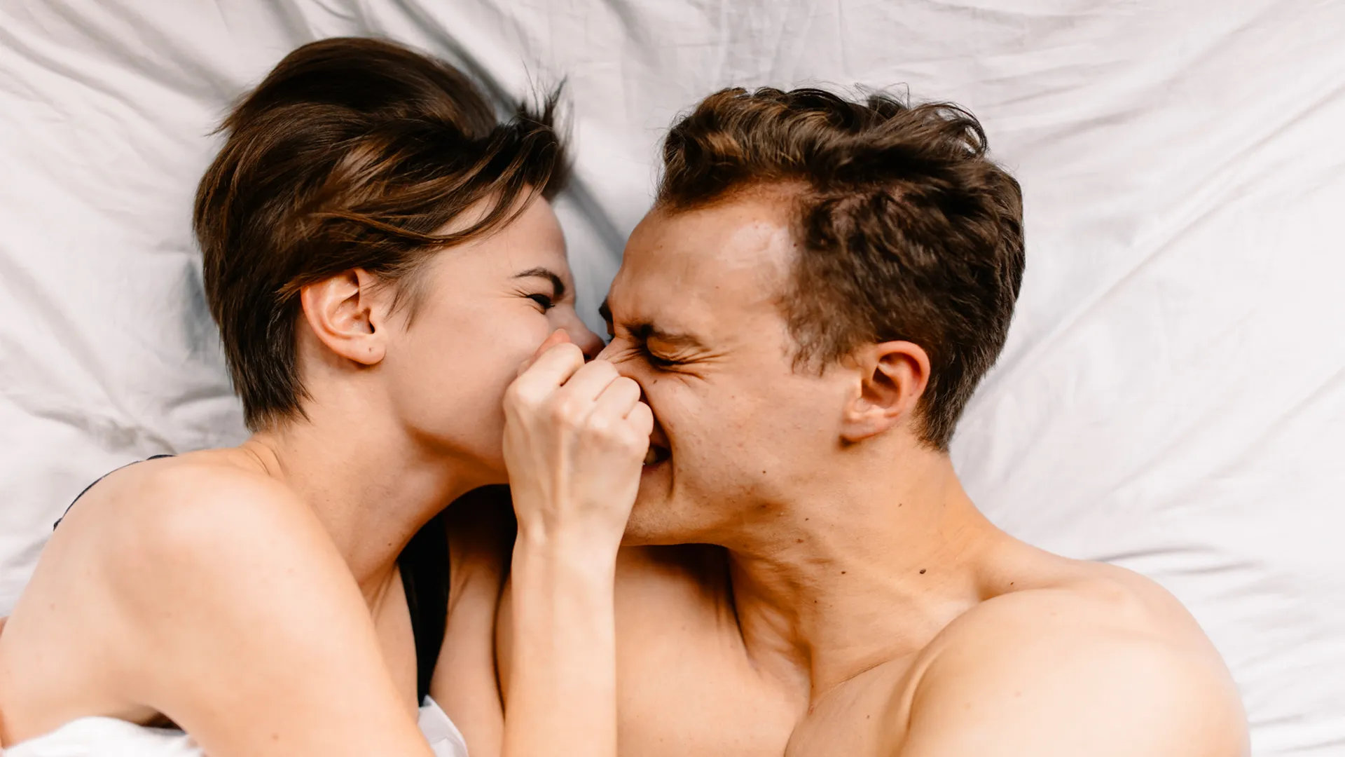 Young couple laughs and shares an affectionate moment while lying in bed together.